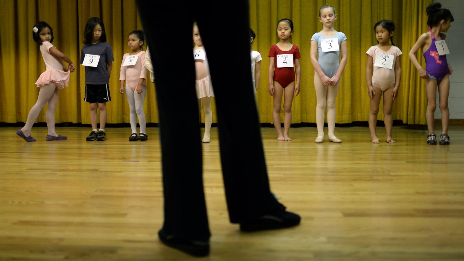 A teacher stands before a class of child ballerinas during an audition.